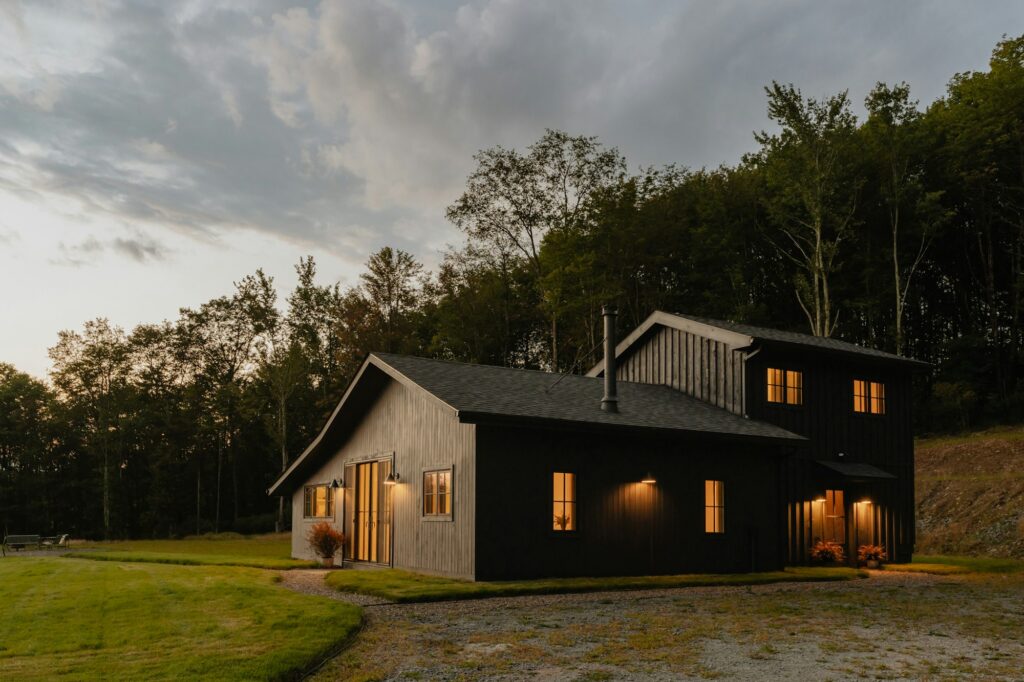 A dark single-story home on a wide green field under a cloudy sky