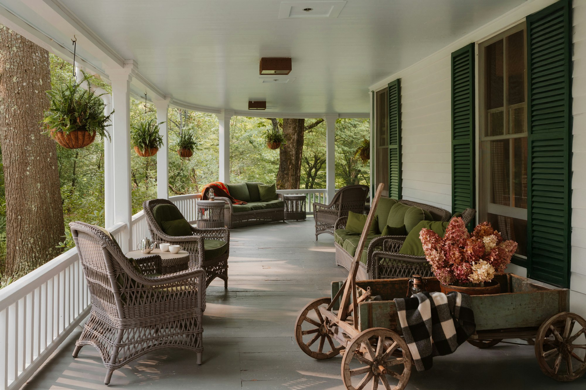 A wide covered porch with wicker chairs and hanging plants