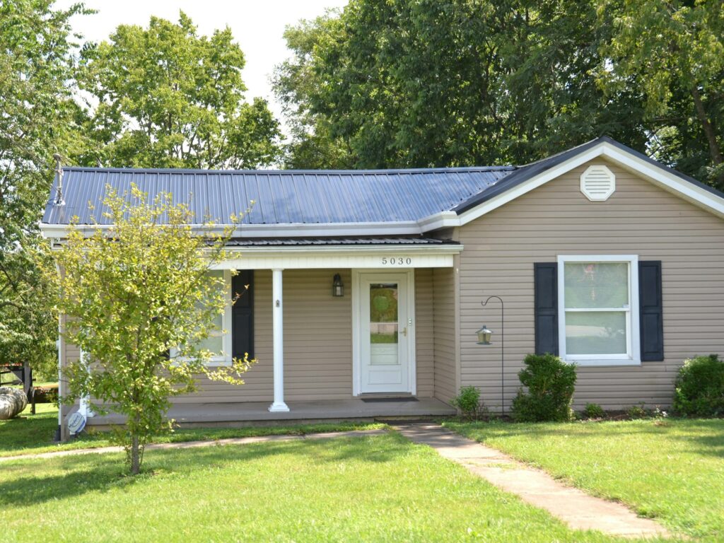 A single-story home with beige siding, a porch and a metal roof
